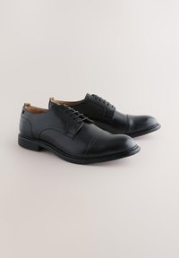 Chaussures en cuir noir à finition lisse, avec des lacets, un bout arrondi et des détails de couture subtils sur le dessus et les côtés.
