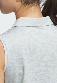Light grey sleeveless polo shirt with a textured pattern. Features a collar and a subtle Adidas logo near the neck. Smooth fabric.