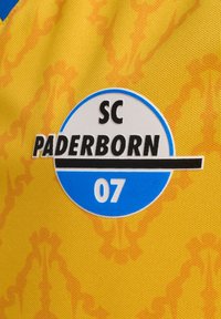 Gul sportströja med ett strukturerat mönster. Har en rund logotyp i blått och vitt som säger "SC PADERBORN 07" med svarta detaljer.