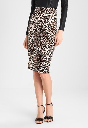 Kvinde iført en høj talje leopard-print pencilnederdel med en sort langærmet top og sorte højhælede sandaler med nitter på stropperne.