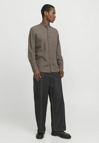 Long-sleeve, collared shirt in muted brown fabric, paired with wide-leg dark denim pants featuring contrasting stitching, and black ankle boots.