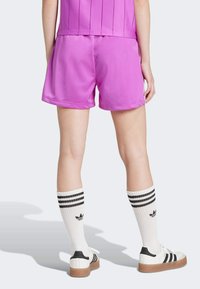 Roze atletske kratke hlače od glatkog, laganog materijala s elastičnom gumom u struku. Nosene s bijelim čarapama s crnim prugama i cipelama s crnim akcentima.