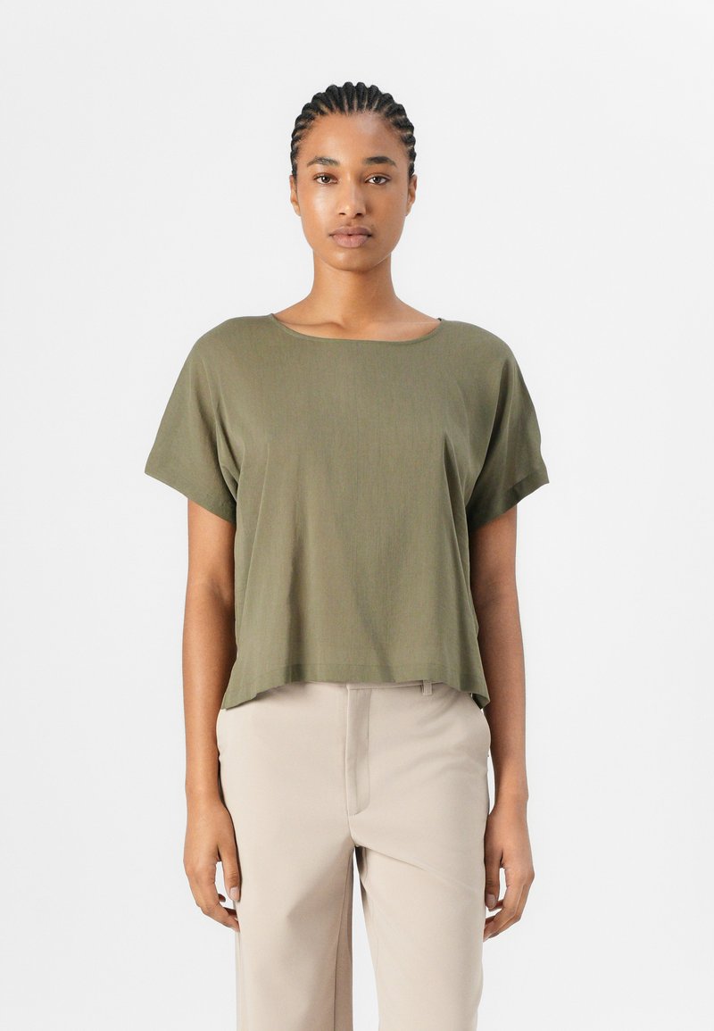 Top corto verde oliva con scollatura quadrata e vestibilità comoda, realizzato in un tessuto morbido e liscio, abbinato a pantaloni beige.