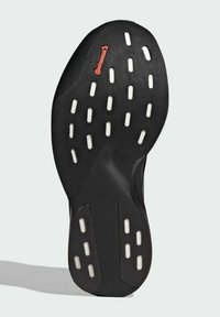 Suela de zapato de goma negra con una superficie texturizada que presenta puntos de tracción blancos y el logotipo "Continental" en naranja. Forma curva con bordes definidos.