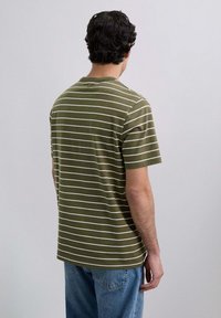 Camiseta de rayas verde olivo hecha de algodón, con rayas horizontales blancas, mangas cortas y cuello redondo. Combinada con jeans azules.