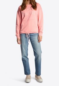 Sudadera rosa con el texto "C'est la vie", con dobladillo y cintura elásticos, bolsillo frontal, combinada con jeans rectos de color azul claro y zapatos beige.