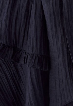 Mekko, jossa on laivastonsininen, ryppyinen kangas ja röyhelöhelma. Ominaisuudet pehmeä tekstuuri ja virtaava muotoilu. Lähikuva tuo esiin monimutkaisia yksityiskohtia.