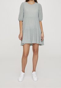 Vestido azul claro, a la altura de la rodilla, con mangas abullonadas, tejido texturizado y diseño con volantes. Combinado con zapatillas blancas.