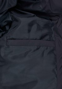 Tela de nailon negra con una textura suave y un bolsillo rectangular simple integrado en el diseño, con detalles de costura sutiles.