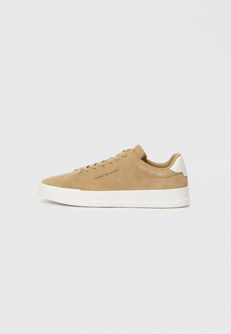 Sneakers in suede beige con suola in gomma bianca, punta rotonda, lacci piatti e un logo discreto sul lato. Texture liscia e design minimalista.