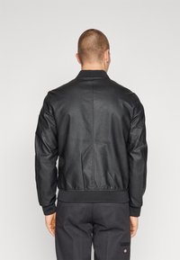 Schwarze Leder-Bomberjacke mit geripptem Kragen und Bündchen, ausgestattet mit einem Reißverschluss und einer strukturierten Oberfläche. Die Rückansicht zeigt klare Linien und Nähte.