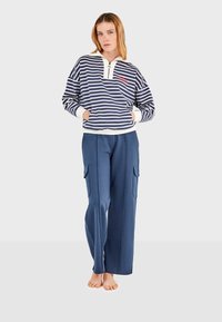 Prugasti dukserica u mornarsko plavoj i bijeloj boji s četvrtim zipom i prednjim džepovima, uparen s širokim mornarsko plavim hlačama s bočnim džepovima za teret.