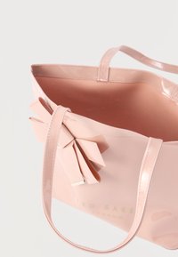 Ροζ, γυαλιστερή τσάντα ώμου με μεγάλο φιόγκο και δύο λαβές. Εσωτερικό μονόχρωμο ροζ χωρίς επιπλέον θήκες. Ορατό το λογότυπο της μάρκας.
