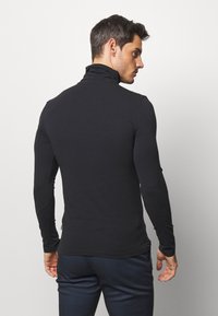 Camiseta negra de manga larga con cuello alto, hecha de una tela suave. Diseño ajustado que resalta el torso, con detalles de costura mínimos visibles.