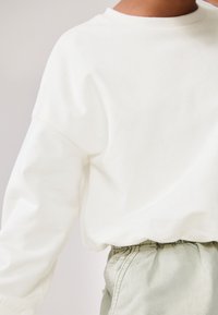 Sweat-shirt blanc en coton doux avec un col rond, présentant des épaules légèrement tombantes et une coupe décontractée, associé à un pantalon vert clair à taille élastique.