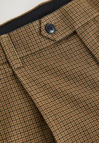 Brown check-patterned fabric with a textured surface, featuring a dark button at the waist and black interior lining.