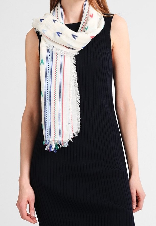 Femme portant une robe noire sans manches côtelée et une écharpe blanche avec des cœurs multicolores et des rayures, les extrémités à franges pendantes à l'avant.