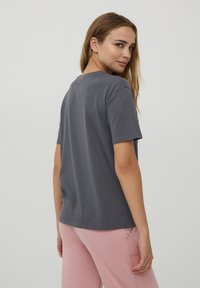 T-shirt grigio a maniche corte in tessuto morbido, caratterizzato da un classico collo tondo e una vestibilità rilassata. Texture liscia senza motivi o dettagli visibili.