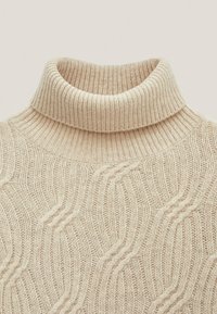 Beiger, gestrickter Rollkragenpullover mit einem strukturierten Wellenmuster und einem gerippten Kragen. Der Stoff wirkt weich und besitzt eine leichte Struktur.