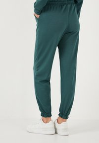 Pantaloni jogger turchesi realizzati in tessuto morbido, con vita elasticizzata, tasche laterali e polsini affusolati, abbinati a sneaker bianche.