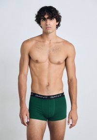 Boxer briefs de algodón verde con una cinturilla elástica negra que presenta el logotipo "GANT" en blanco repetido. Textura suave, diseño ajustado.
