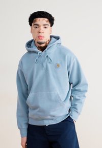Light blue hoodie with a kangaroo pocket, adjustable drawstring hood, and small logo patch on the chest. Soft fabric with a relaxed fit.