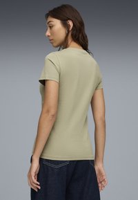 Camiseta de manga corta verde oliva con cuello redondo y diseño ajustado, combinada con jeans de pierna ancha azul oscuro. Tela de algodón suave.