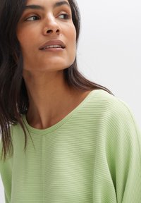 Helles grünes, geripptes Stricktop mit einem weiten Rundhalsausschnitt und weichem Griff, das dezente vertikale Streifen und kurze Ärmel aufweist.
