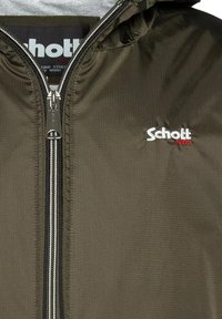 Kurtka przeciwwiatrowa w oliwkowym kolorze, wykonana z lekkiego materiału, z pełnym zamkiem błyskawicznym i regulowanym kapturem. Posiada logo "Schott NYC" w białym i czerwonym kolorze.