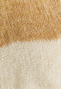 Knitted fabric swatch featuring two horizontal stripes; top in light golden brown, bottom in off-white, with a soft, fluffy texture.