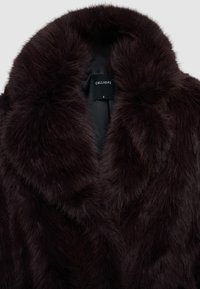 Dunkelbrauner, plüschiger Kunstfellmantel mit breitem Reverskragen und schwarzem Innenfutter, das ein kleines "Calliope"-Etikett zeigt.