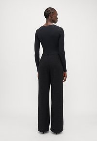 Black long-sleeve bodysuit with ribbed texture paired with high-waisted wide-leg pants in a textured fabric, both in black.