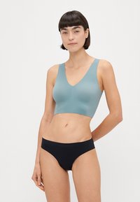 V-hals bralette i blødt teal materiale, sømløs design, parret med sorte hipster trusser. Glat tekstur, minimalistisk stil, ingen synlig hardware.