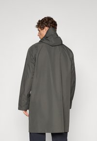 Abrigo gris impermeable con capucha, con un corte recto, tejido ligeramente texturizado y mangas largas. Sin hardware ni patrones visibles.