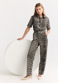 Conjunto de camisa y pantalones con estampado de leopardo, confeccionado en tela texturada. Colores negro y beige, con mangas cortas, cierre frontal de botones y diseño de pierna recta.