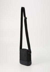 Black crossbody bag with a textured fabric upper and smooth, matte base. Features a sturdy adjustable strap and a snap buckle closure.