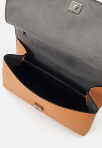 Borsa a tracolla in pelle color tan con una finitura liscia e un interno in suede grigio. Presenta una chiusura a pulsante argento e un design compatto.