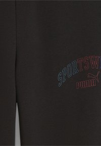 Pantalones deportivos de algodón negros con un logo en texto azul y rojo que dice "SPORTSWEAR" y "PUMA" en un diseño curvado. Textura suave.