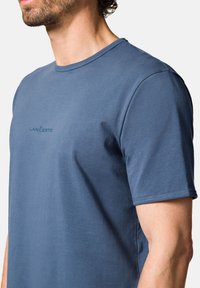 Męska koszulka z krótkim rękawem w jednolitym niebieskim kolorze, wykonana z bawełny. Posiada okrągły dekolt oraz subtelne haftowane logo na piersi. Gładka tekstura.