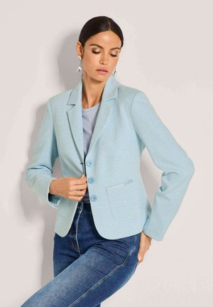 Hellblauer, strukturierter Blazer mit tailliertem Design, Reverskragen, drei Knöpfen und Seitentaschen, kombiniert mit einem grauen Oberteil und Jeans.