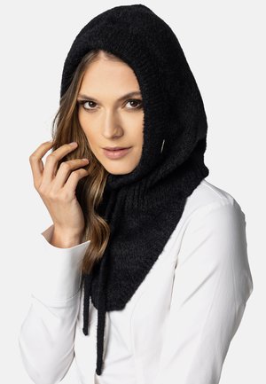 Sciarpa con cappuccio nera lavorata a maglia, con una finitura morbida e testurizzata, dotata di lacci regolabili e forma a imbuto. Indossata sopra una camicia bianca.