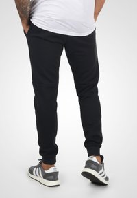 Sorte tapered sweatpants lavet af blødt stof med sidelommer og ribbede manchetter, parret med grå sneakers med hvide striber.