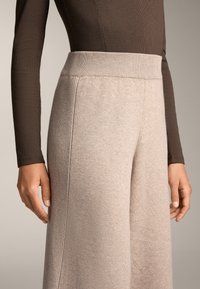 Beige, vida stickade byxor med en ribbad midje. Tyget är texturerat och mjukt, med sidoseams för en skräddarsydd passform.