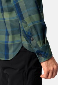 Camisa de manga larga a cuadros en verde y azul con puños abotonados. La tela parece suave con un ligero brillo. Presenta un dobladillo en punta y una costura diagonal en las mangas.