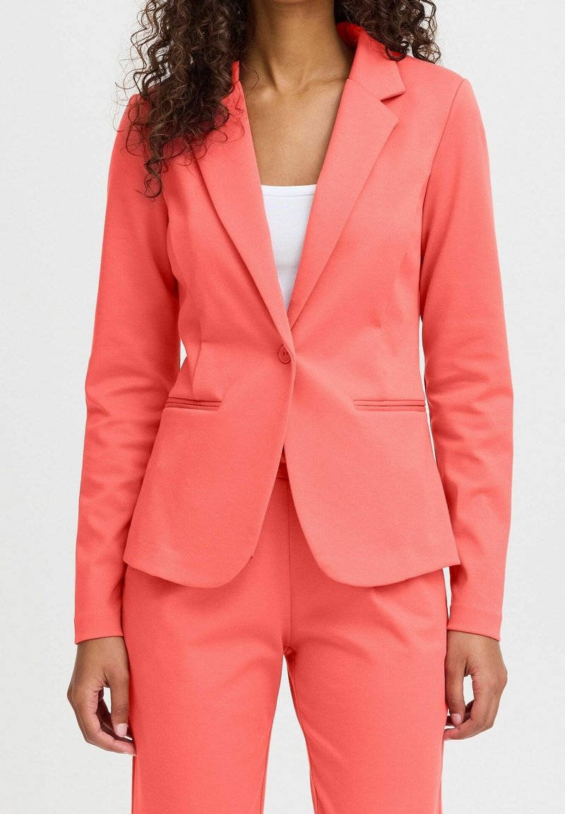 Blazer corail à coupe ajustée, fermeture à un bouton, revers à encoches et deux poches latérales, confectionné dans un tissu lisse et extensible.
