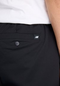 Shorts noirs avec une texture lisse, dotés d'une poche arrière et d'une petite étiquette de logo New Balance. Le design est simple et fonctionnel.