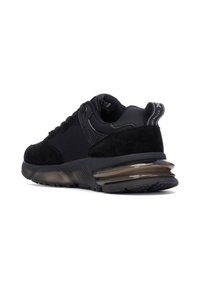 Zapatilla deportiva negra que combina materiales de ante y malla, con una suela gruesa y transparente y acentos texturizados en los lados.