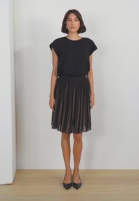 Haut noir à manches courtes associé à une jupe midi plissée noire. La jupe présente une texture lisse et une taille élastique. Escarpins noirs à bout pointu.