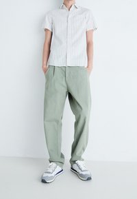 Korte mouwen gestreepte shirt in wit en blauw, lichtgroene broek met een losse pasvorm, en grijze sneakers met witte en marineblauwe accenten.
