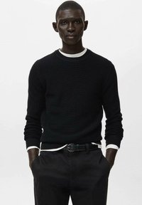 Maglione nero a maglia testurizzata con collo rotondo, bordo interno bianco, abbinato a pantaloni neri e una cintura nera. Design minimalista.